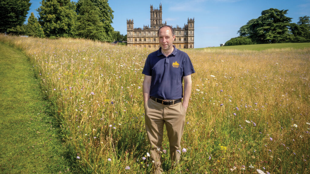 Simon Andrews in a wildflower meadow with a historic country house in the backdrop